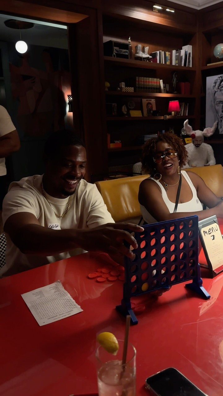 Man and woman playing Connect Four at a red table in a lounge