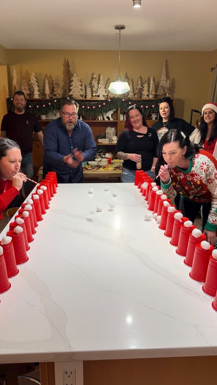 Adults playing a competitive game with red plastic cups on a white kitchen island