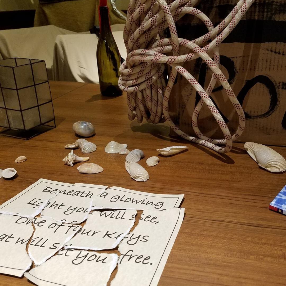 Torn paper with a riddle, seashells, and rope on a wooden table.