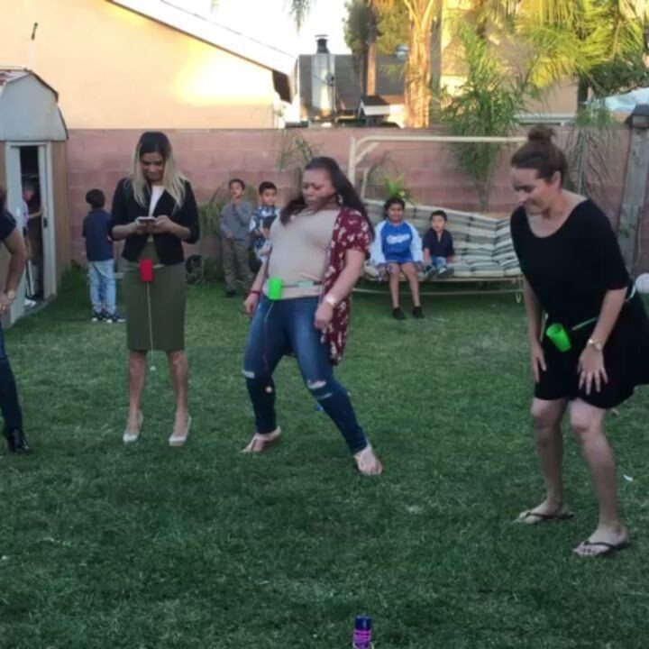 Three women playing a backyard game with green cups attached to their waists.