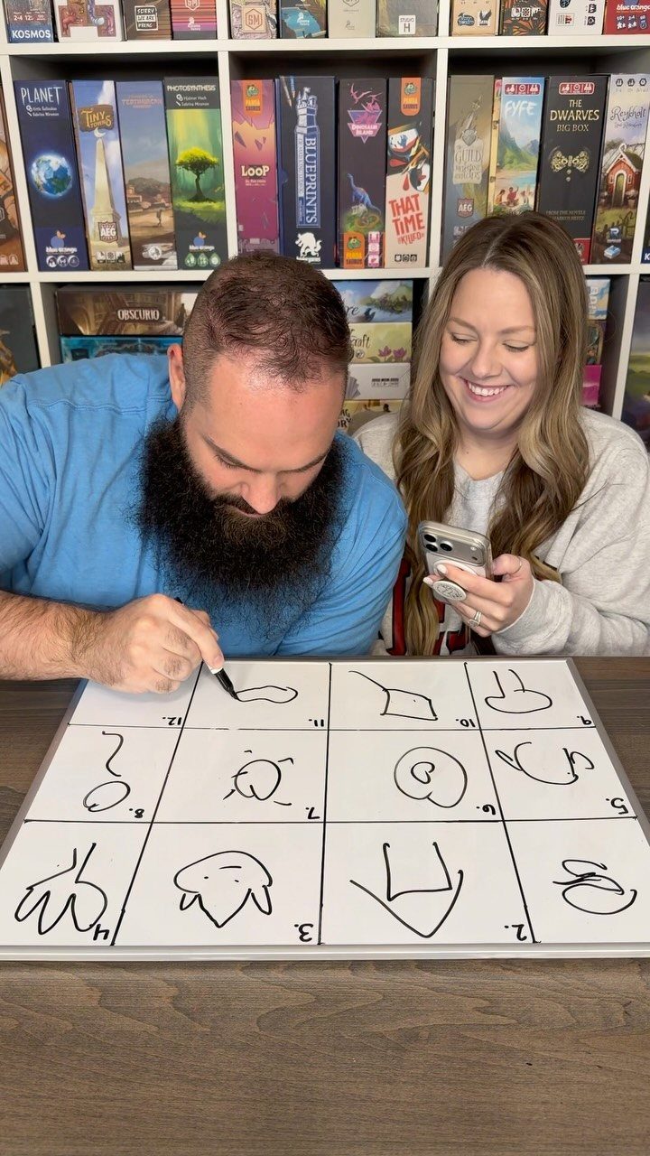 Man drawing on a game board while a woman watches in a game room