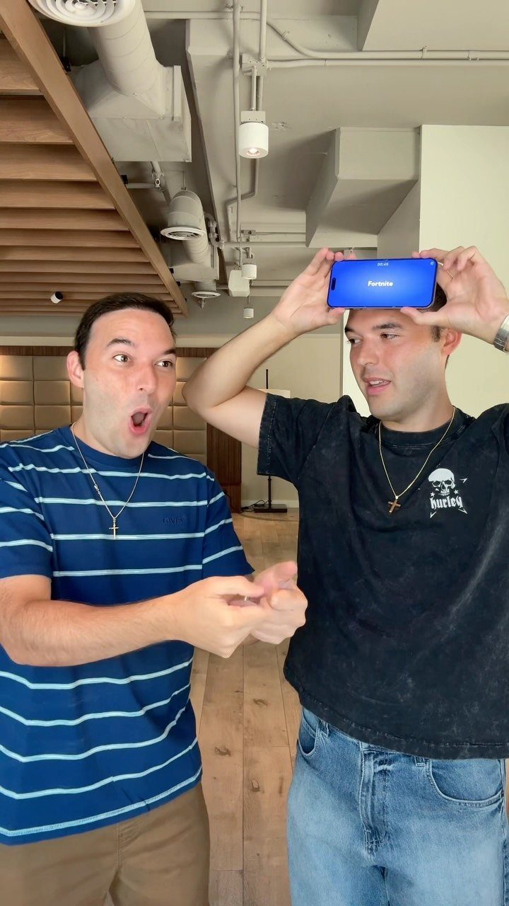 Two men playing a game with a smartphone held against one man's forehead.