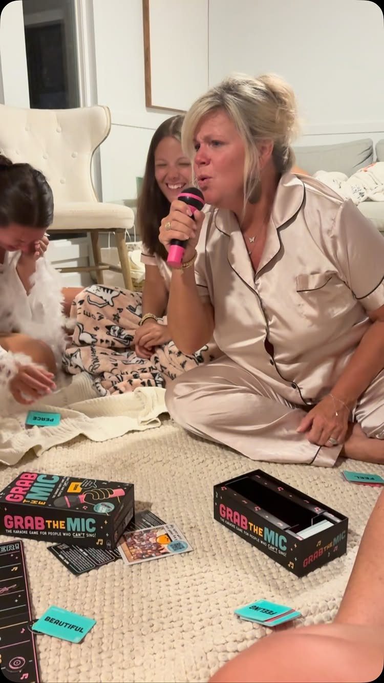 Woman in satin pajamas singing into a pink microphone during a party game.