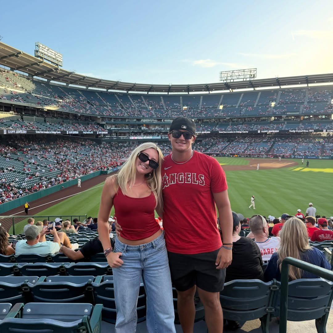 Couple posing in red clothing at a baseball stadium during a live game.