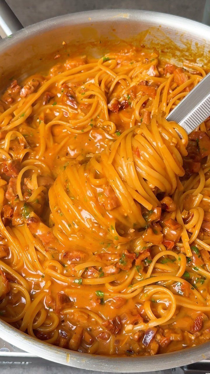 Spaghetti with creamy orange sauce being lifted from a silver metal pan.