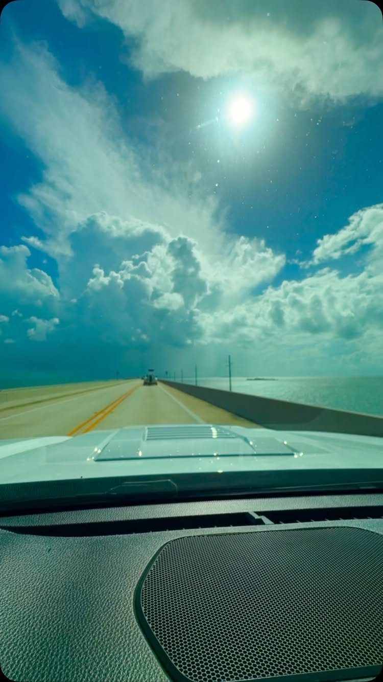 Road stretching toward the horizon viewed from a car dashboard under a sunny sky