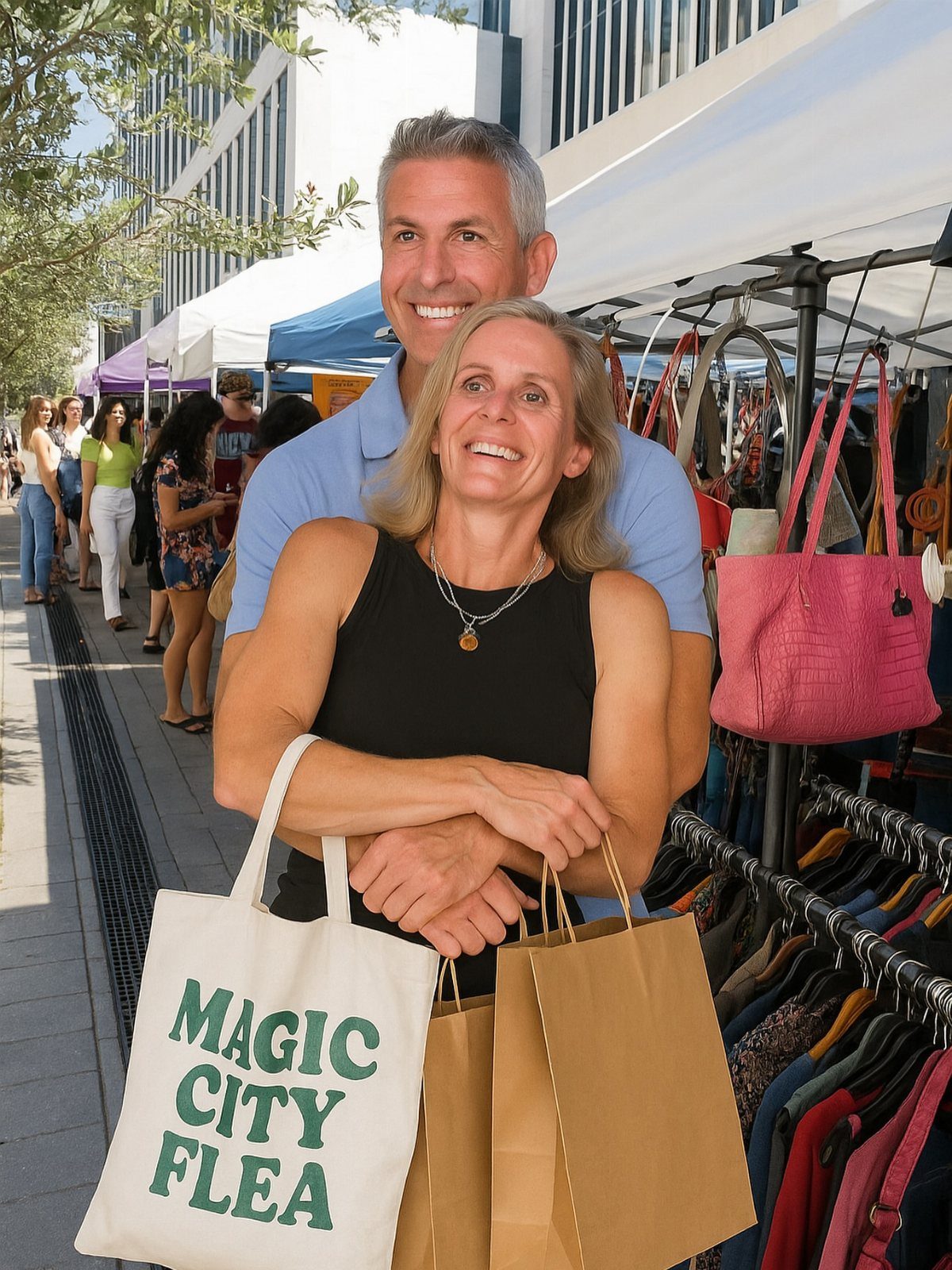 Smiling couple holding shopping bags at an outdoor flea market with clothing racks.