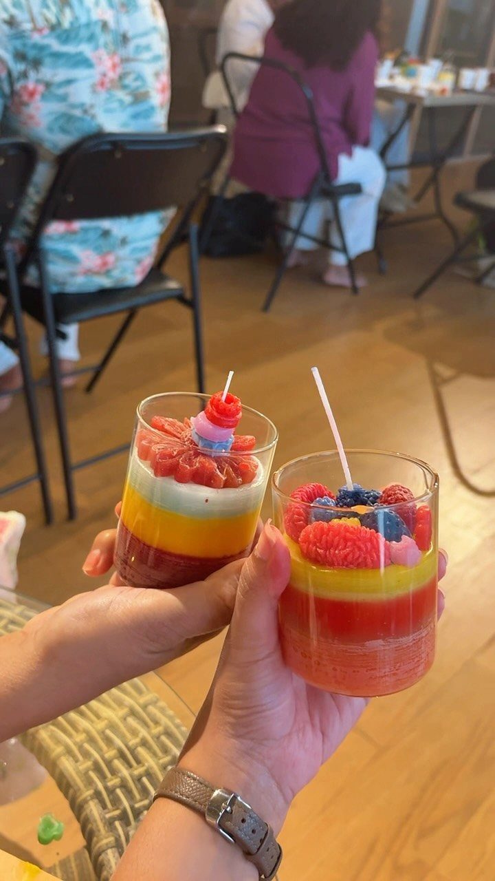 Two hands holding colorful layered dessert candles topped with wax berries.