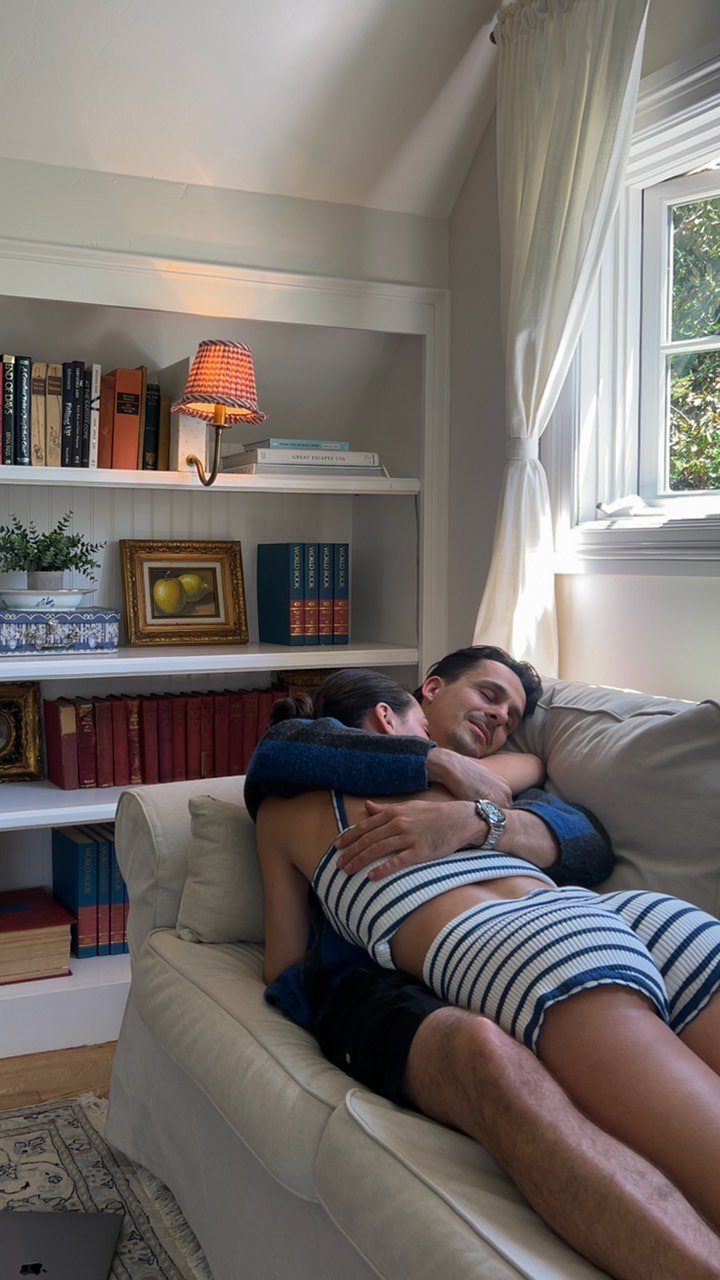 Couple cuddling on a white sofa in a cozy room with bookshelves.