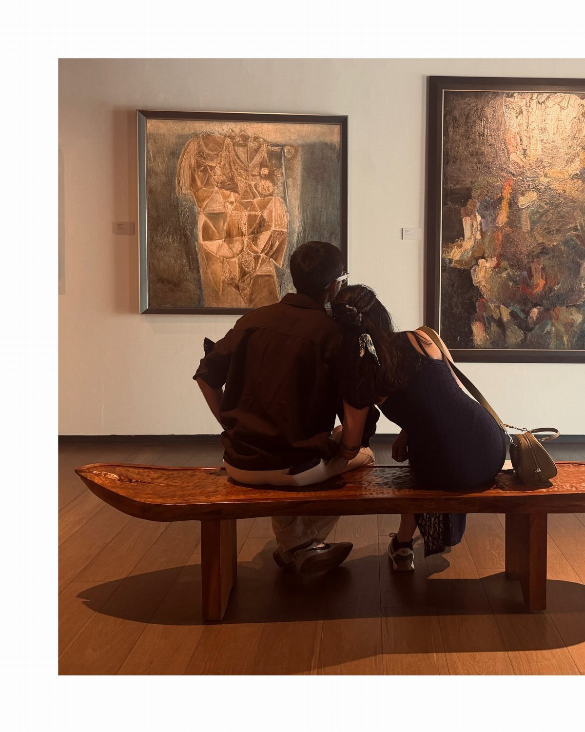 Couple sitting on a wooden bench viewing abstract paintings in an art gallery