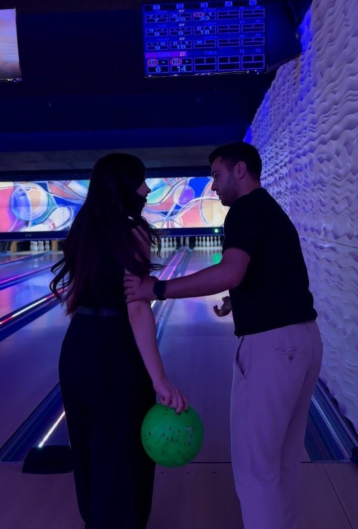 Couple standing on a bowling lane with a green bowling ball and neon lights.