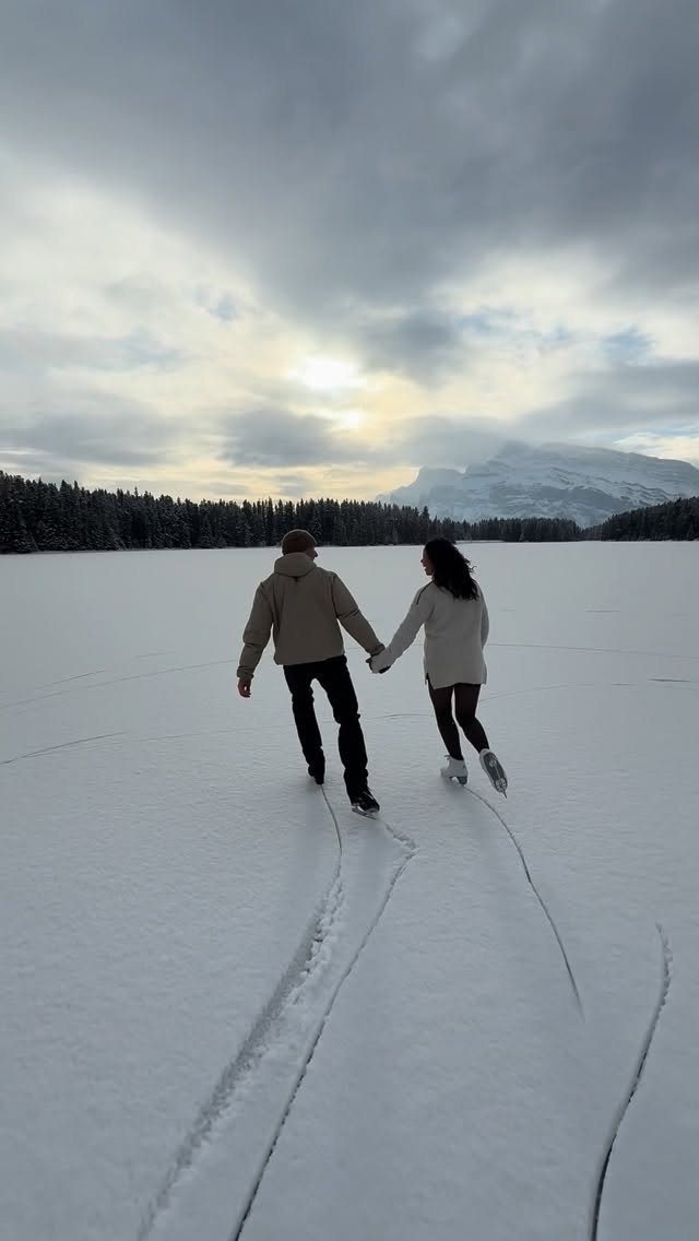 Couple holding hands while ice skating on a frozen lake with mountains behind.