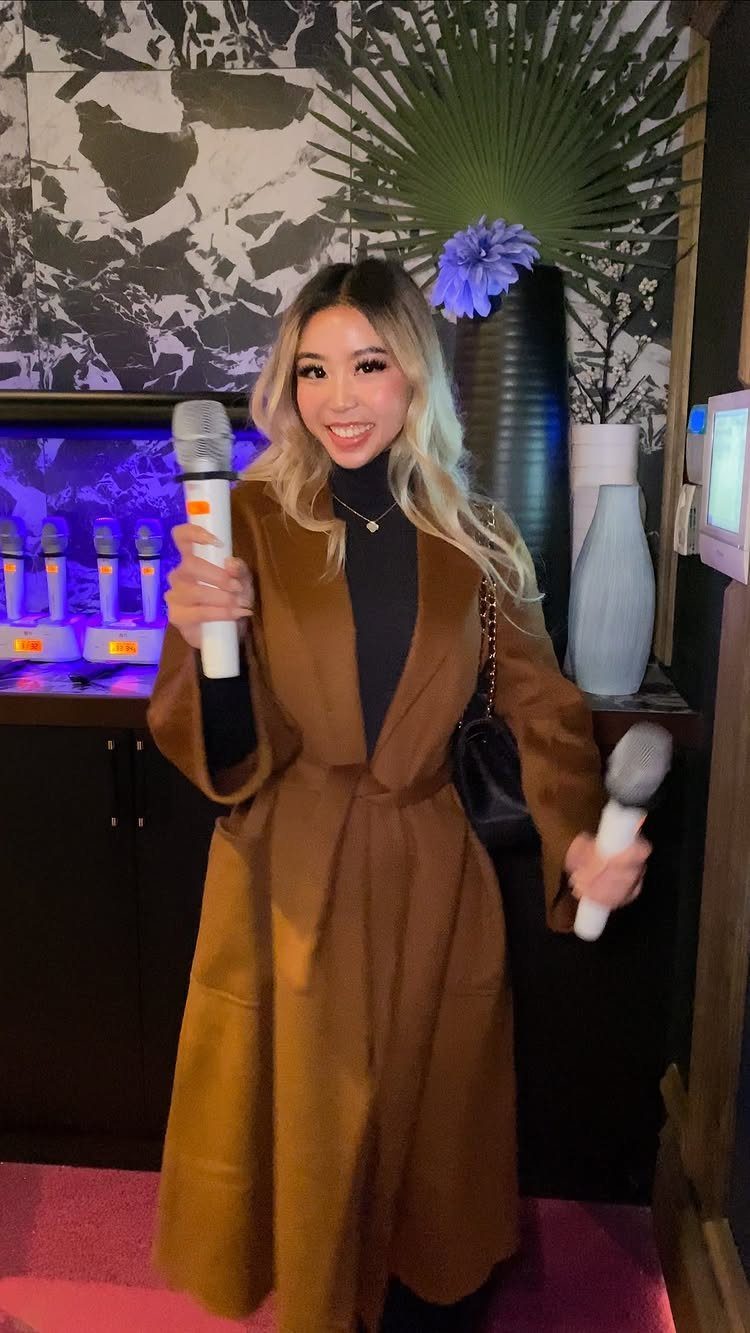 Woman smiling and holding two microphones in a karaoke room setting.