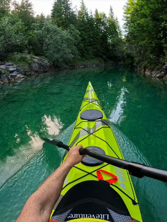 Yellow kayak on clear turquoise water surrounded by a lush green forest.