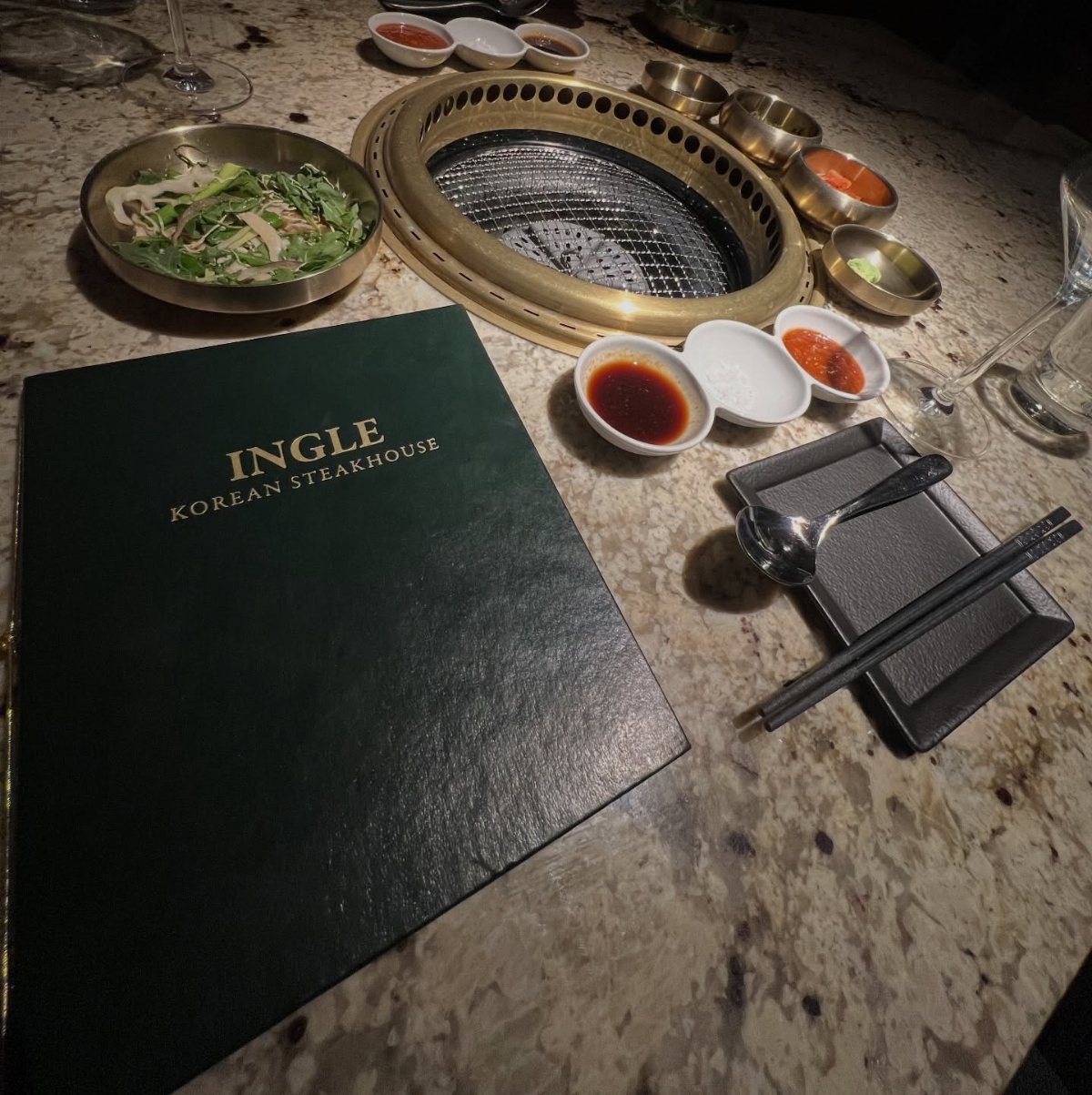 Korean steakhouse table setting with a built-in grill, menu, and side dishes.