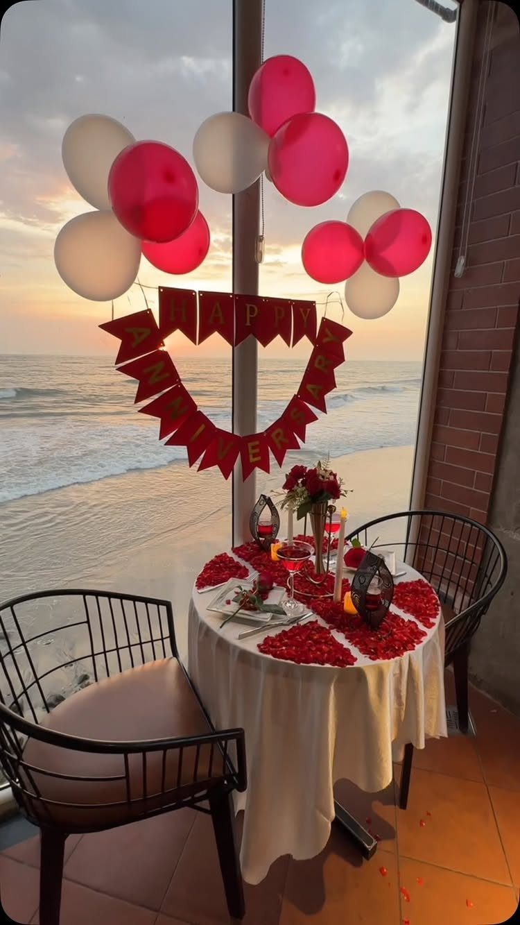 Romantic anniversary dinner table with red rose petals and balloons overlooking the ocean.