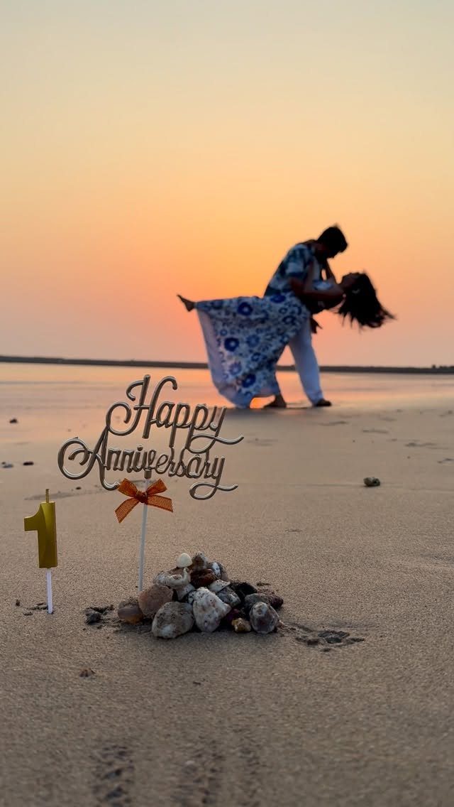 Anniversary cake topper and candle on beach sand with dancing couple at sunset