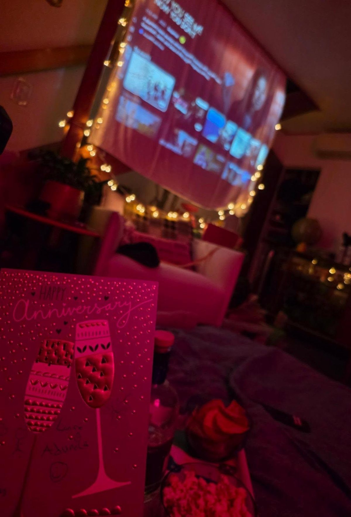 Projector screen with movie menu and fairy lights next to an anniversary card.
