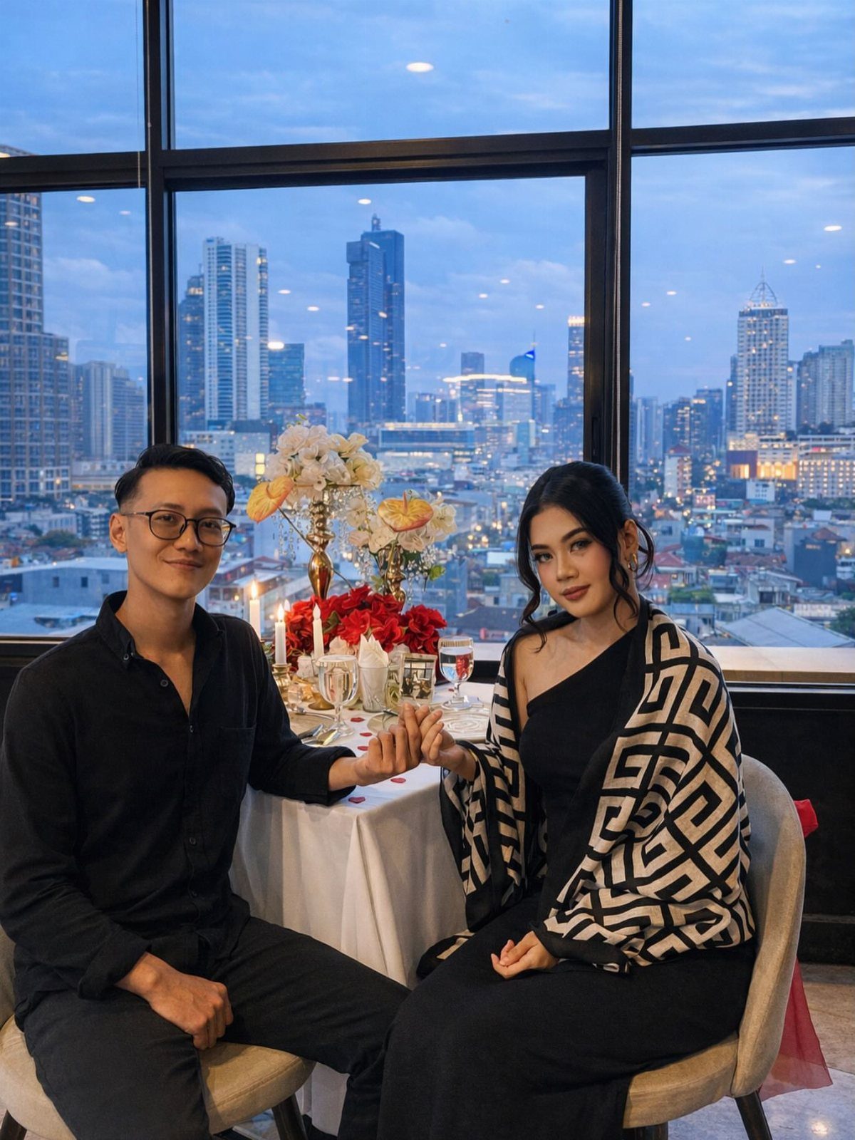 Couple holding hands at a romantic dinner table overlooking a city skyline at dusk.