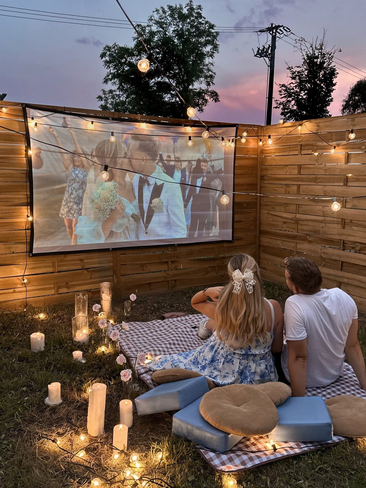 Couple watching a wedding video on an outdoor projector screen with cozy lighting.