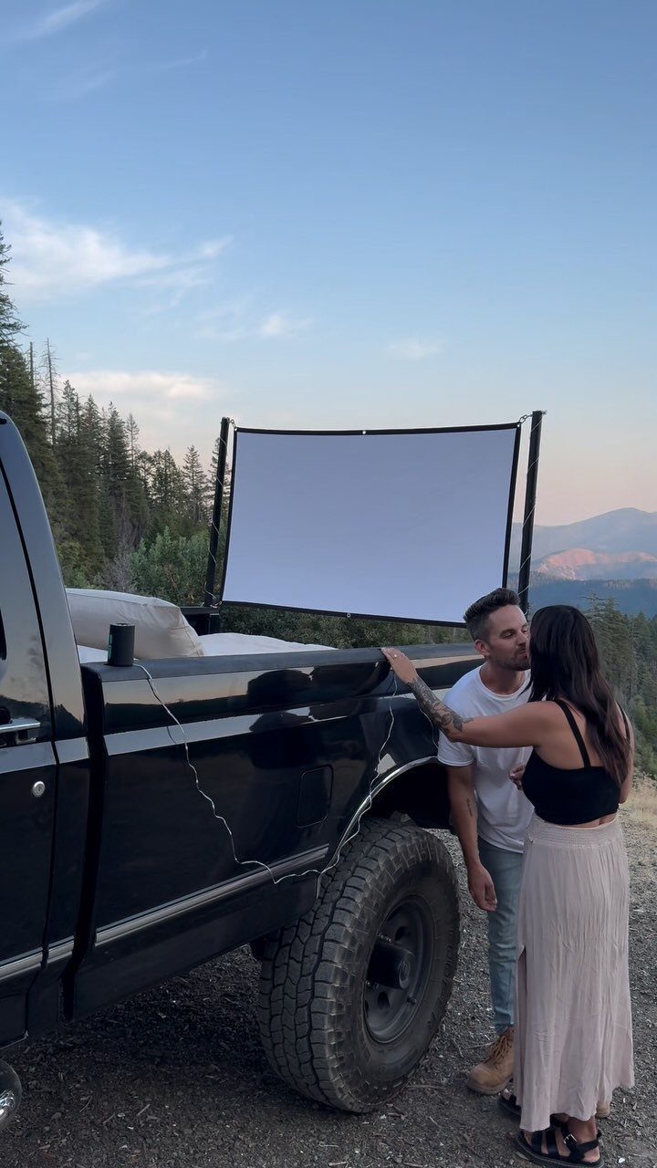 Couple standing by a pickup truck with a projector screen in the bed outdoors.