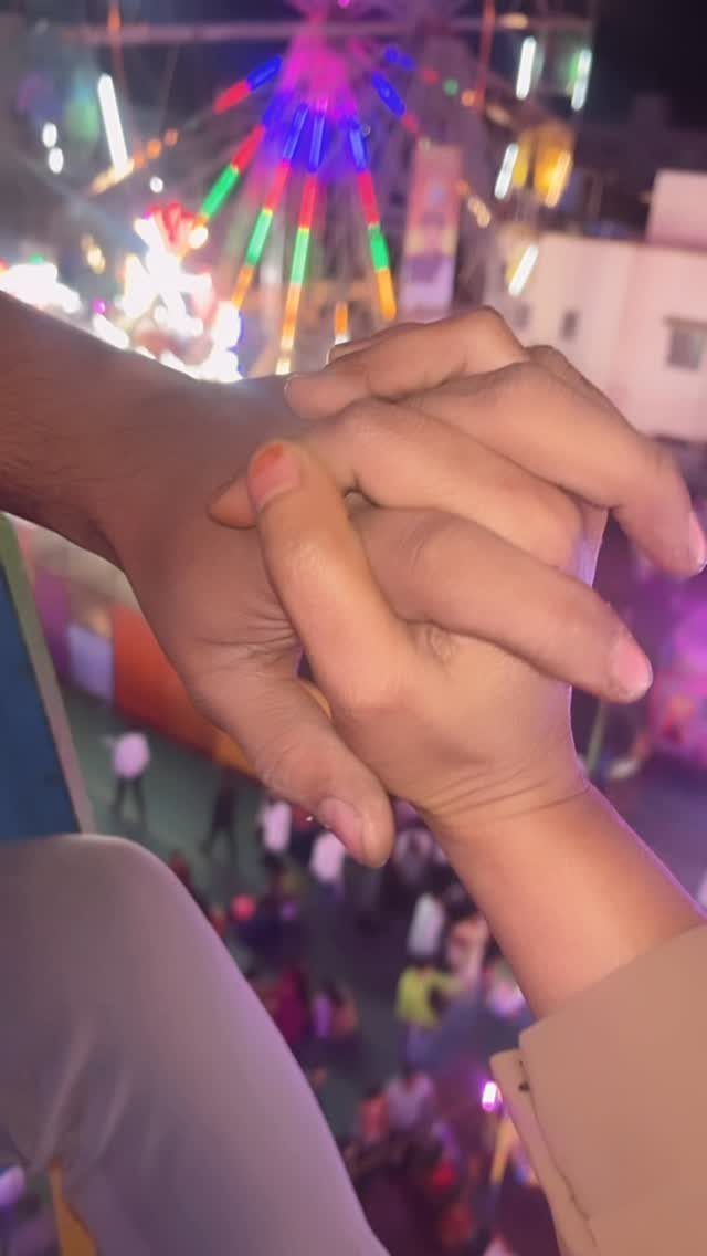 Two people holding hands with a colorful Ferris wheel in the background.