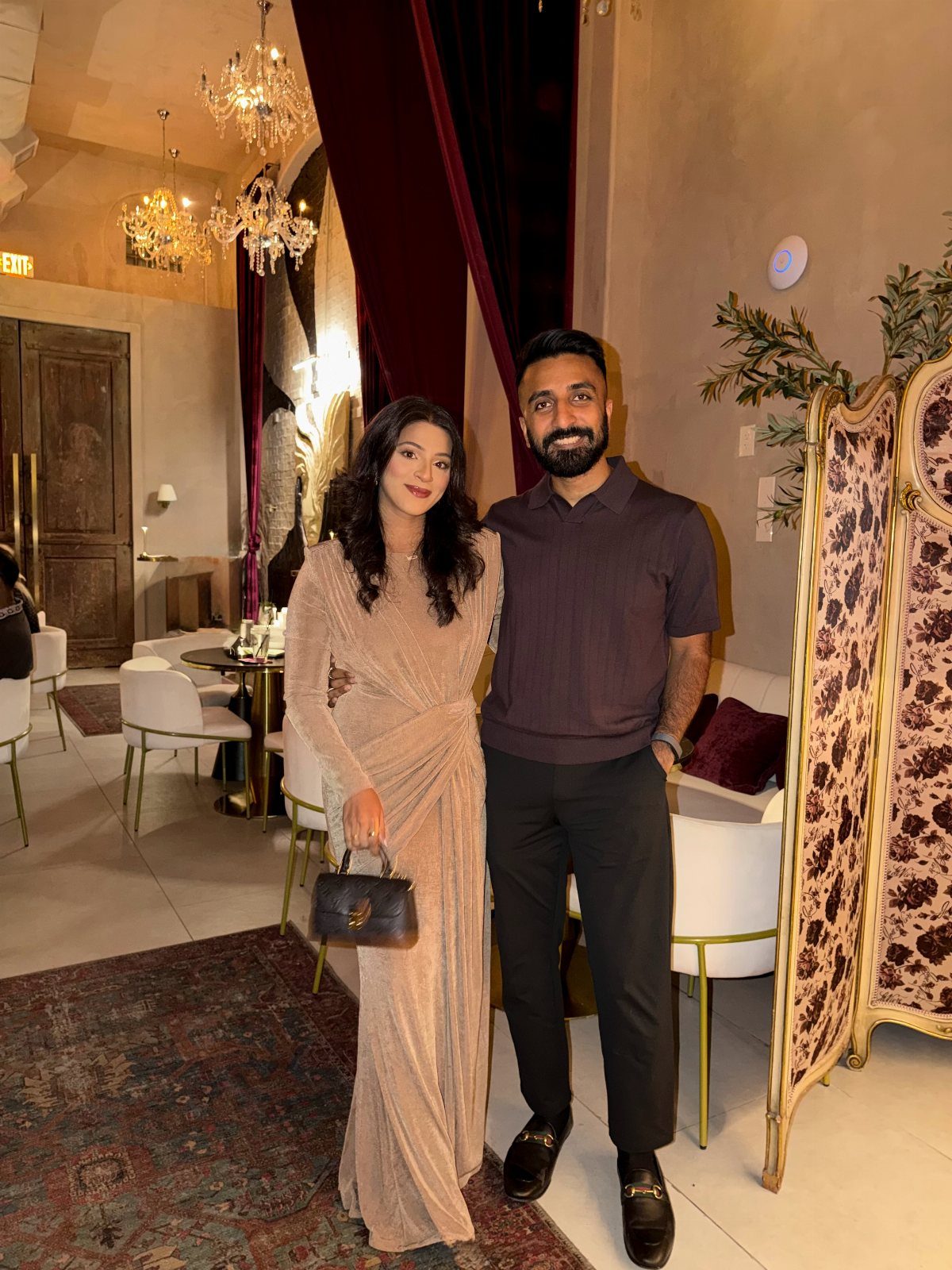 Woman in a champagne ruched jersey dress and man in dark attire posing indoors.
