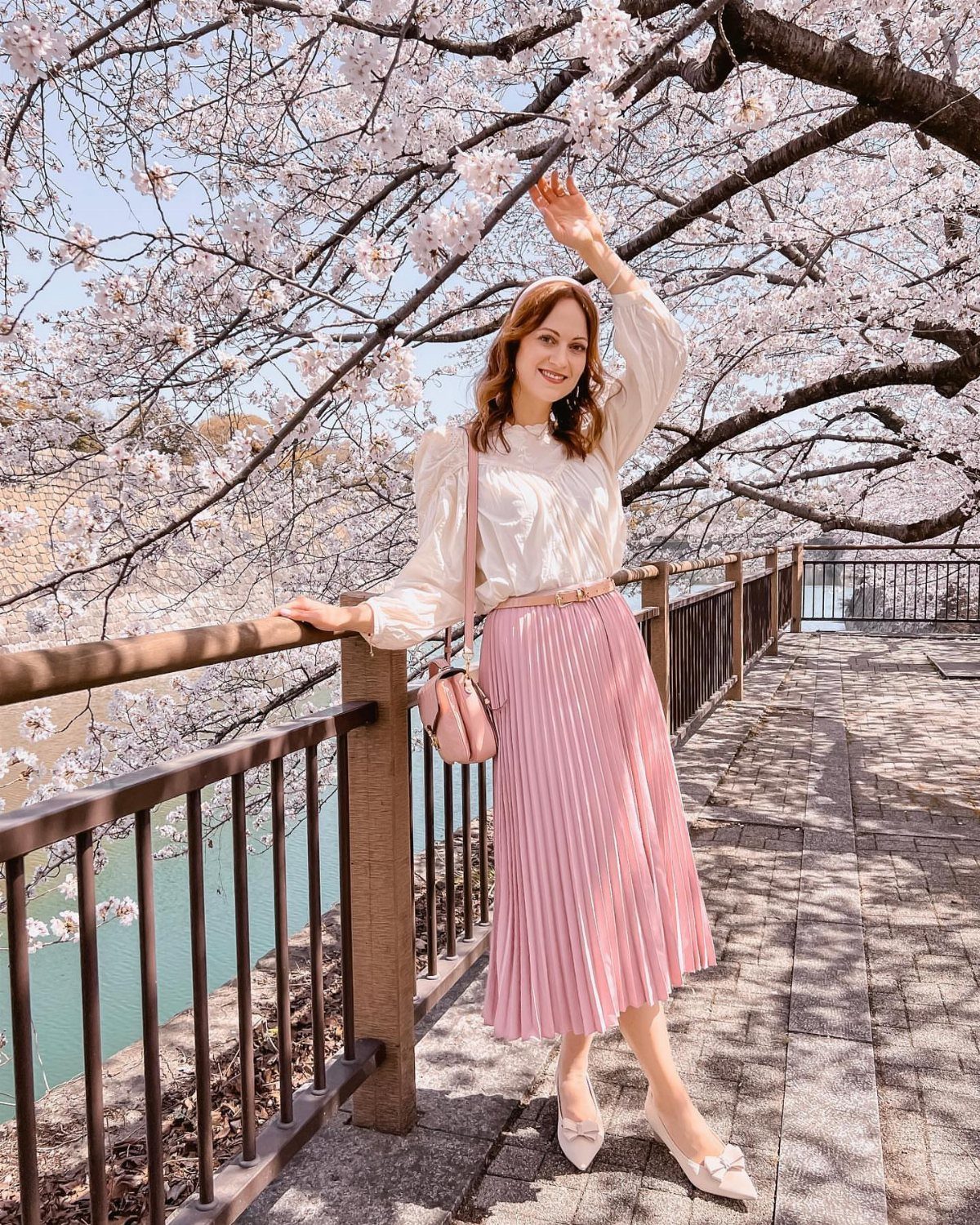 Woman in white blouse and pink pleated midi skirt under cherry blossoms
