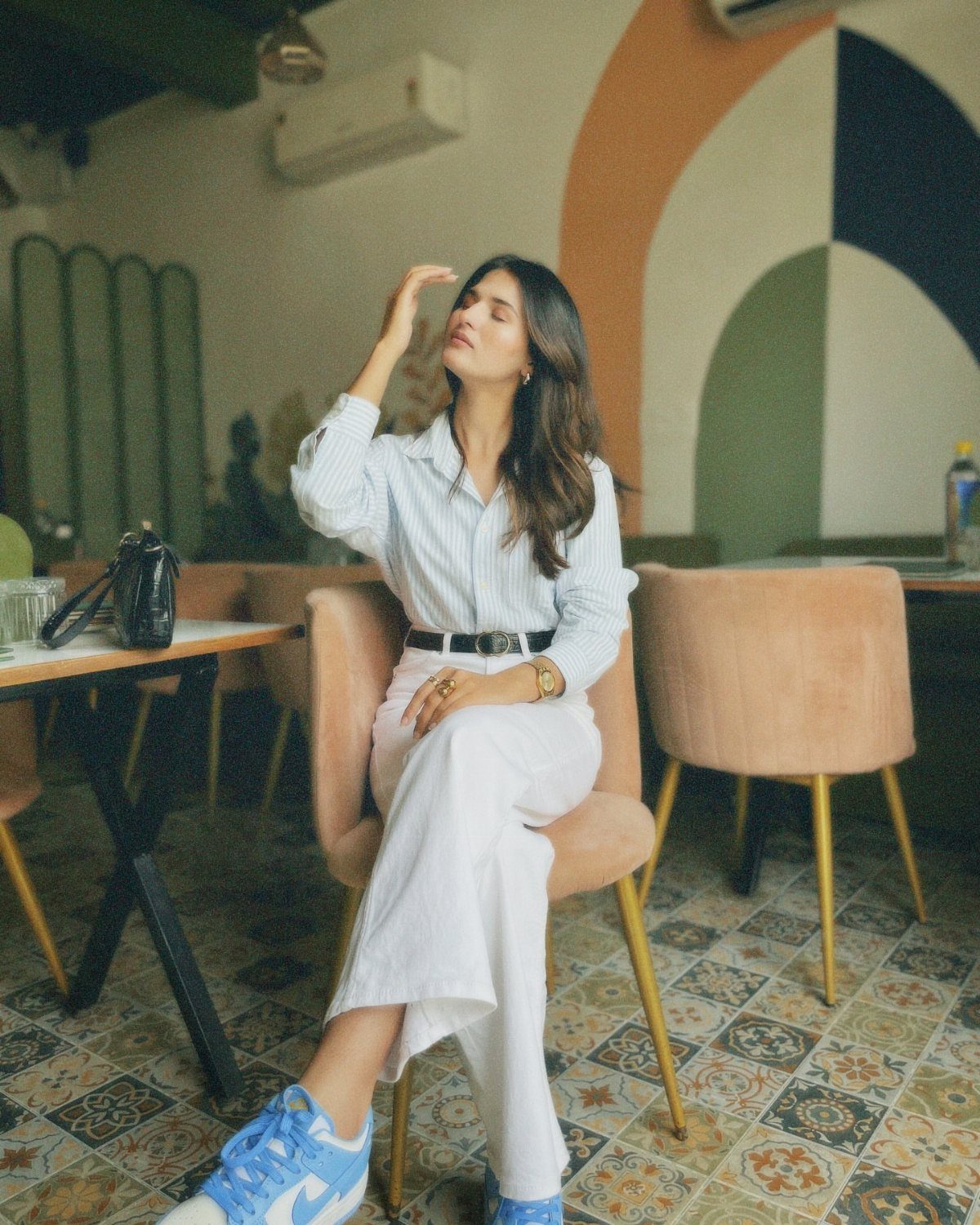 Woman wearing a striped shirt and white trousers sitting in a modern cafe.