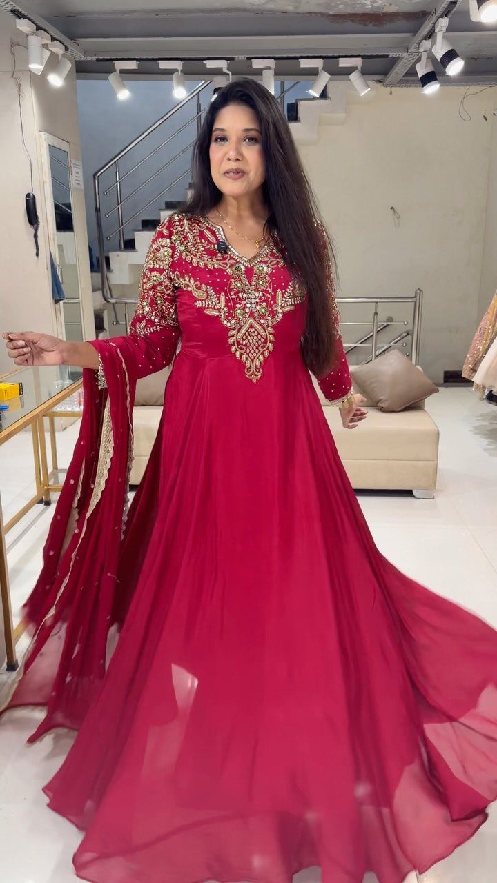 Woman wearing a floor-length deep red gown with gold embroidery in a room.