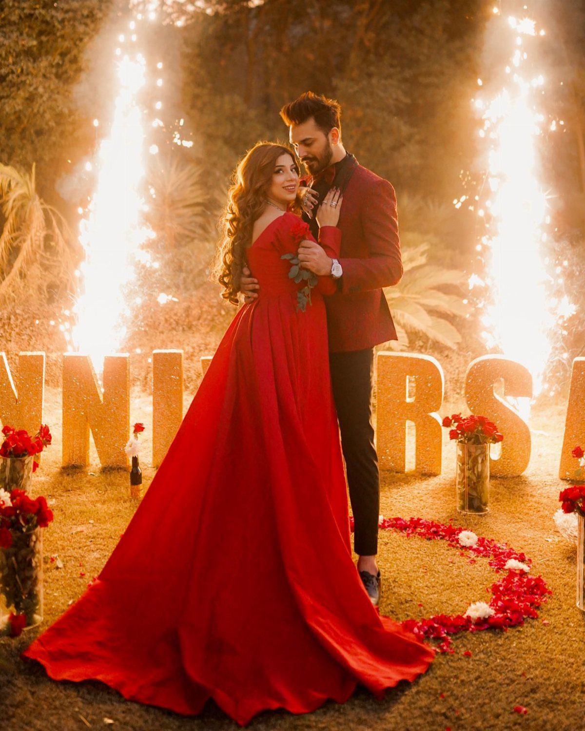 Woman in red floor-length gown and man in red blazer embracing outdoors.