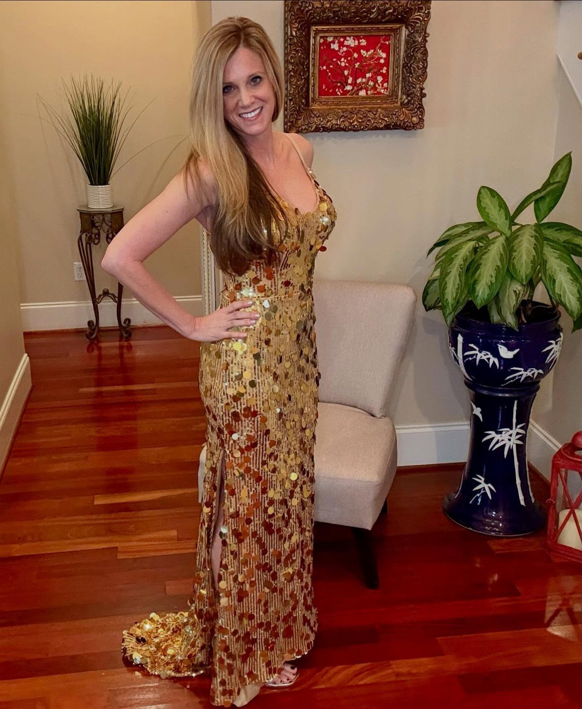 Woman wearing a gold sequined floor-length gown posing in a living room