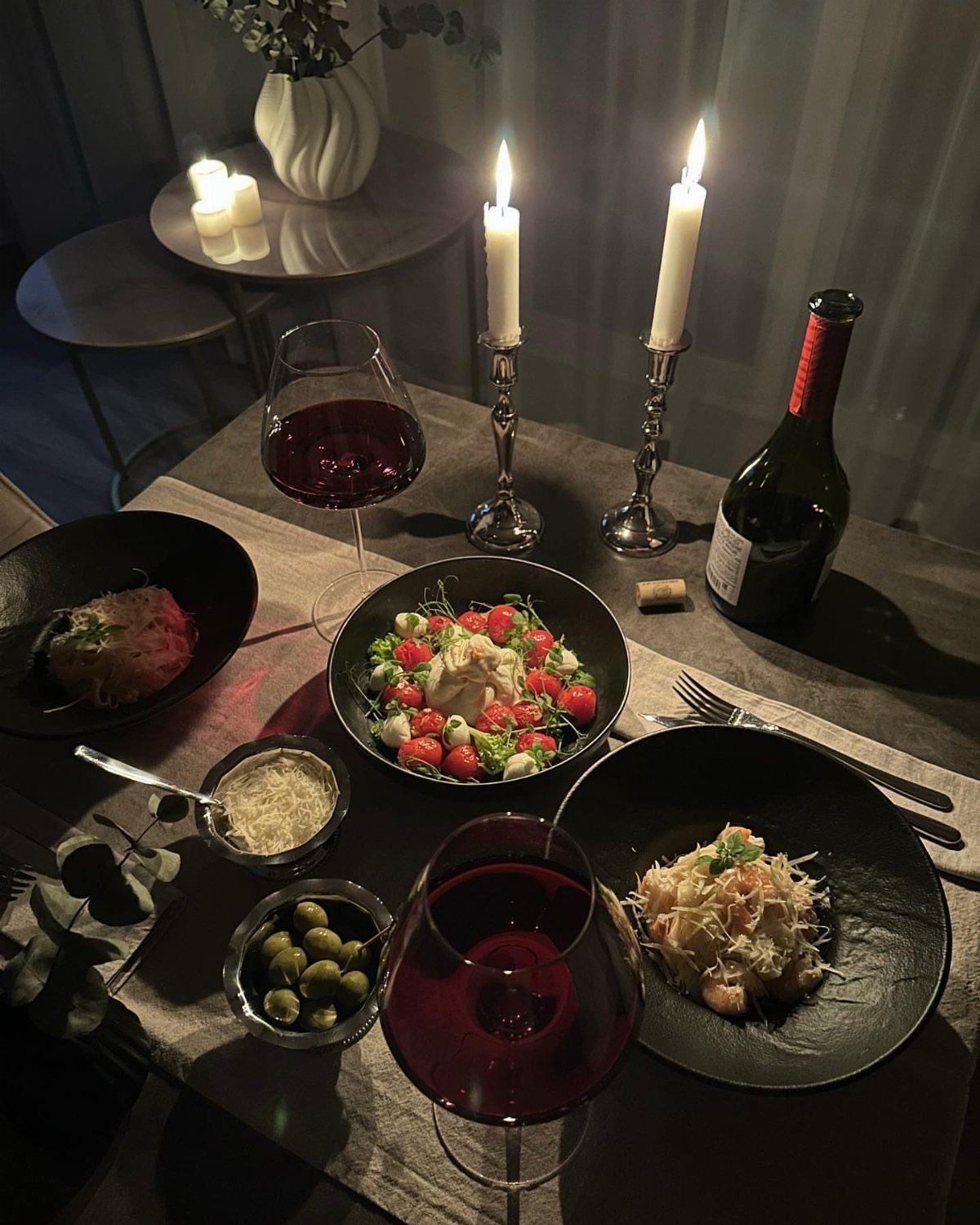 Candlelit dinner table with red wine, gourmet plates, and glowing white taper candles.