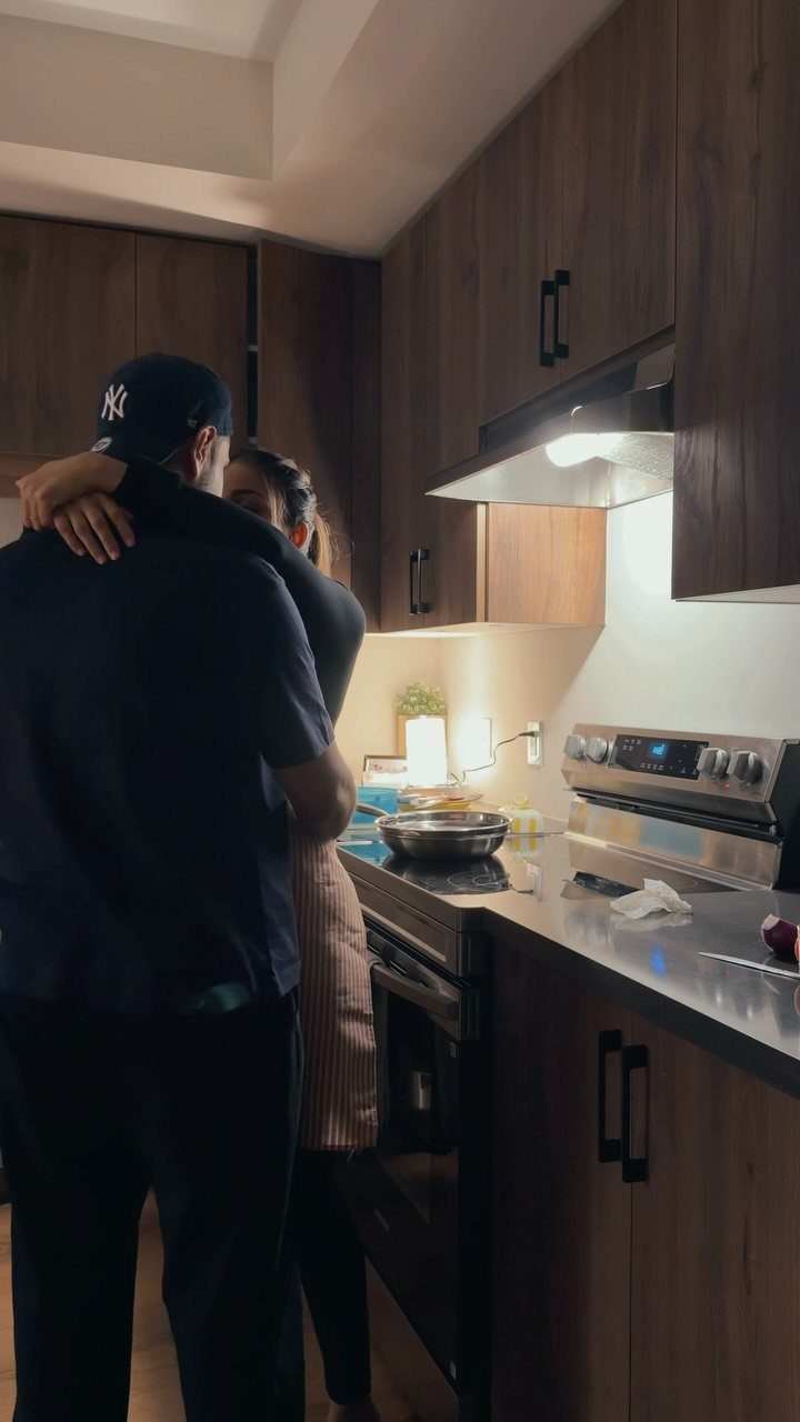 Couple hugging in a kitchen by the stove while preparing a meal together.