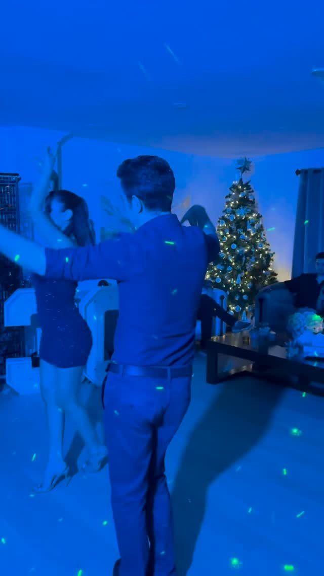 Couple dancing in a living room with blue lighting and a Christmas tree.
