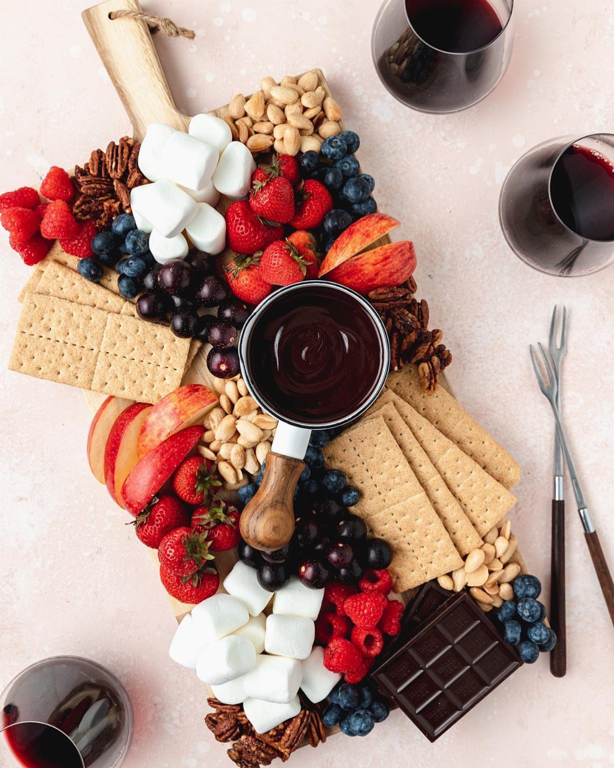 Chocolate fondue pot surrounded by fresh fruit, marshmallows, and crackers with red wine.