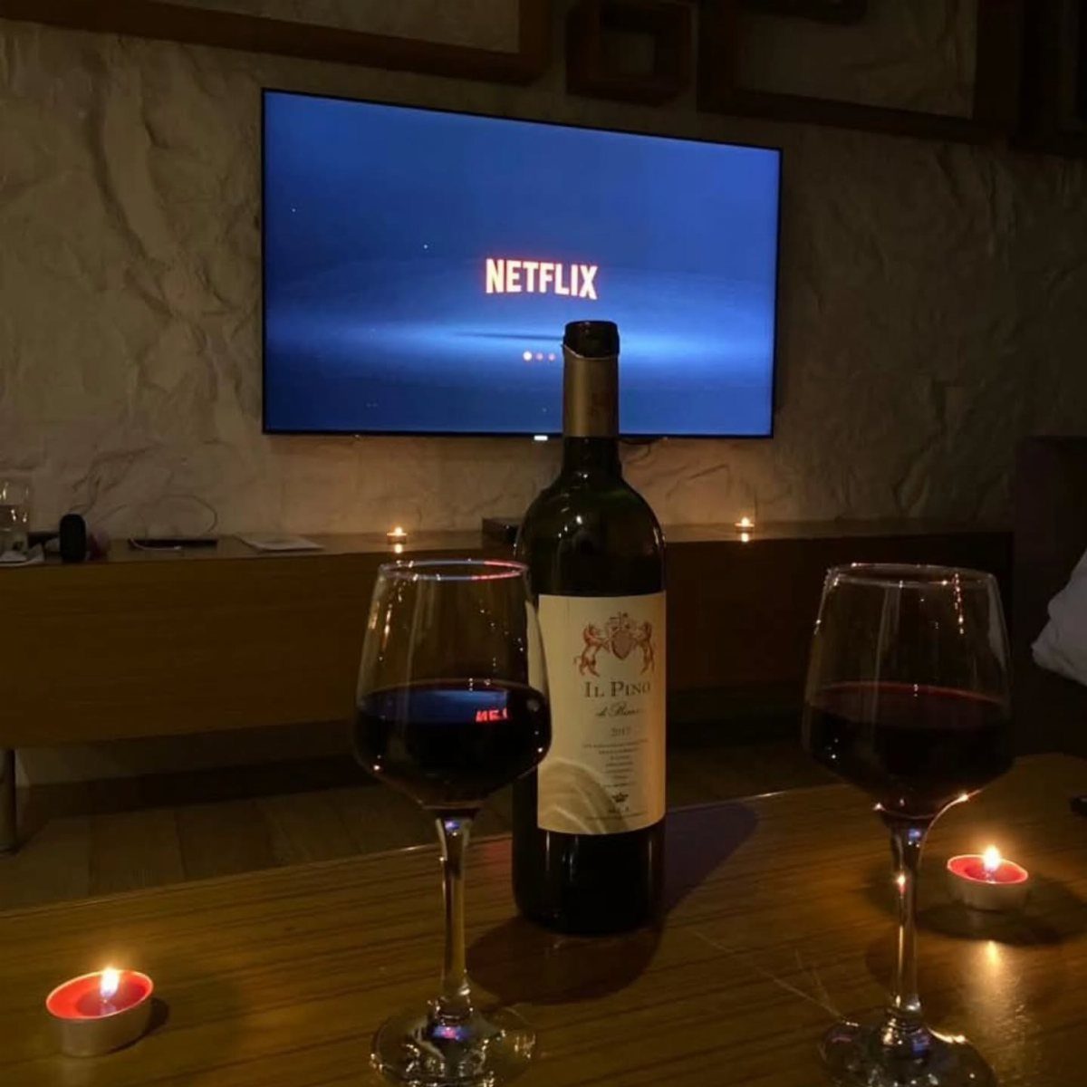 Bottle of red wine and two glasses on a table before a television.