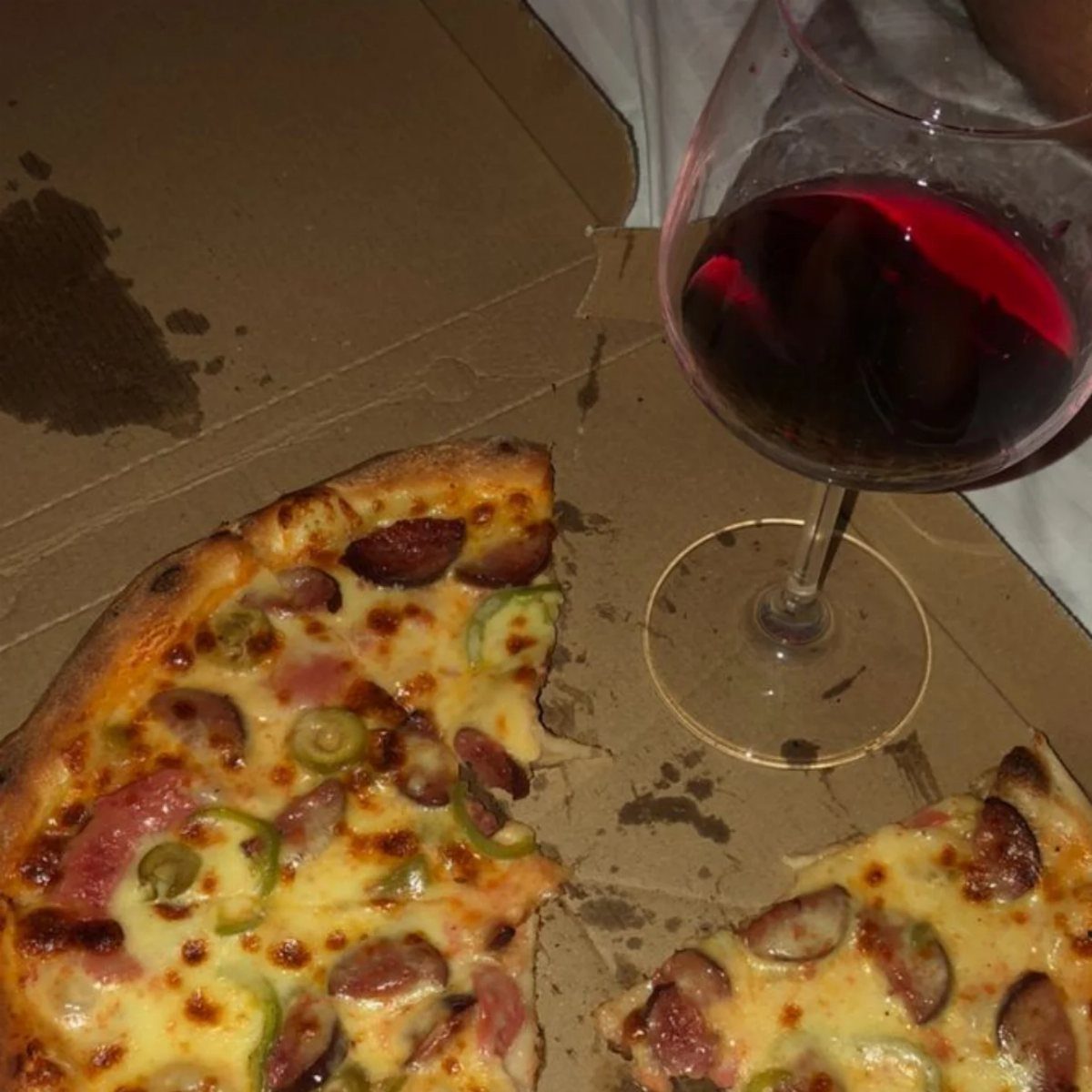 Pizza slices with sausage and peppers in a box next to red wine.