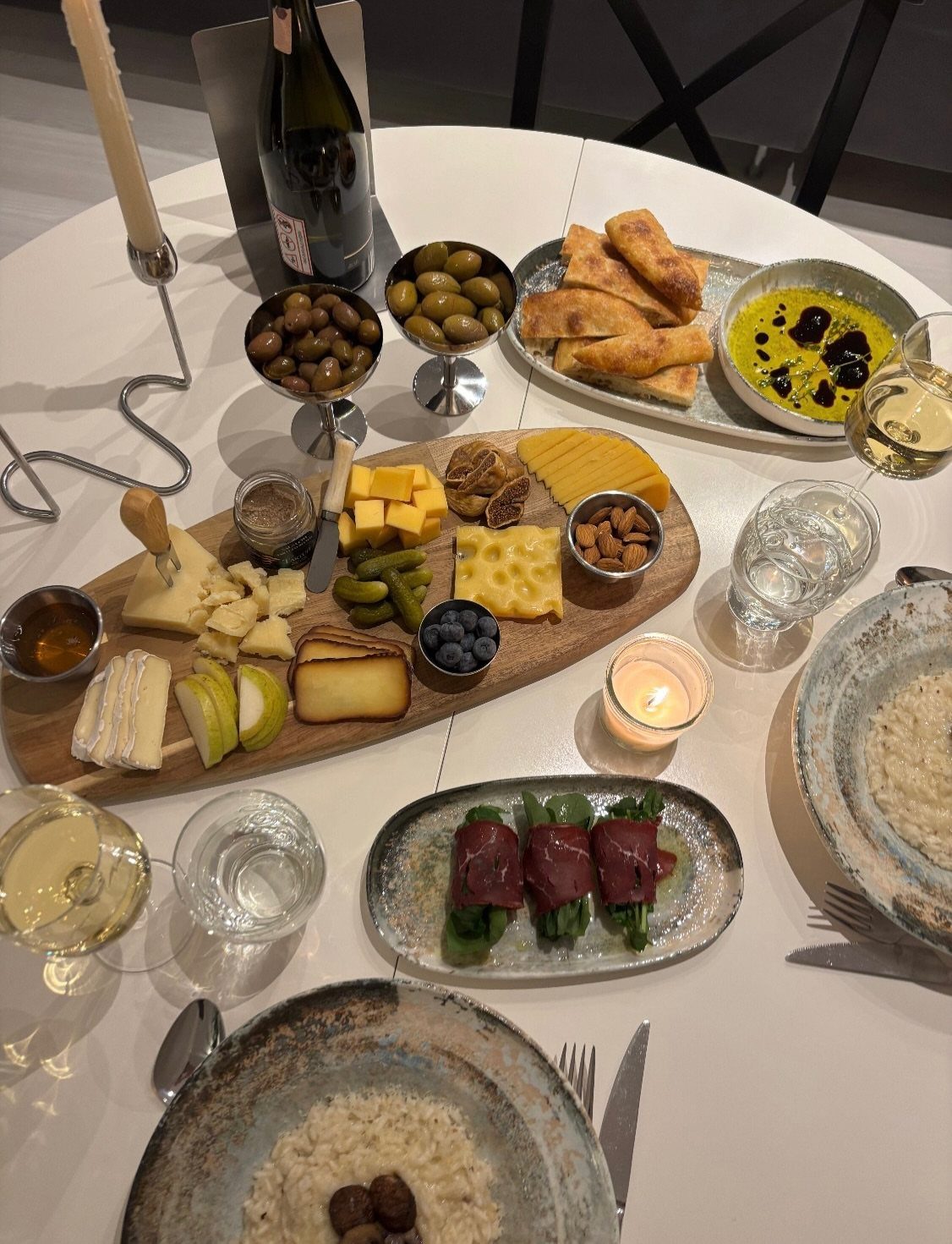 Gourmet spread of cheese, olives, and wine on a white table with candlelight.