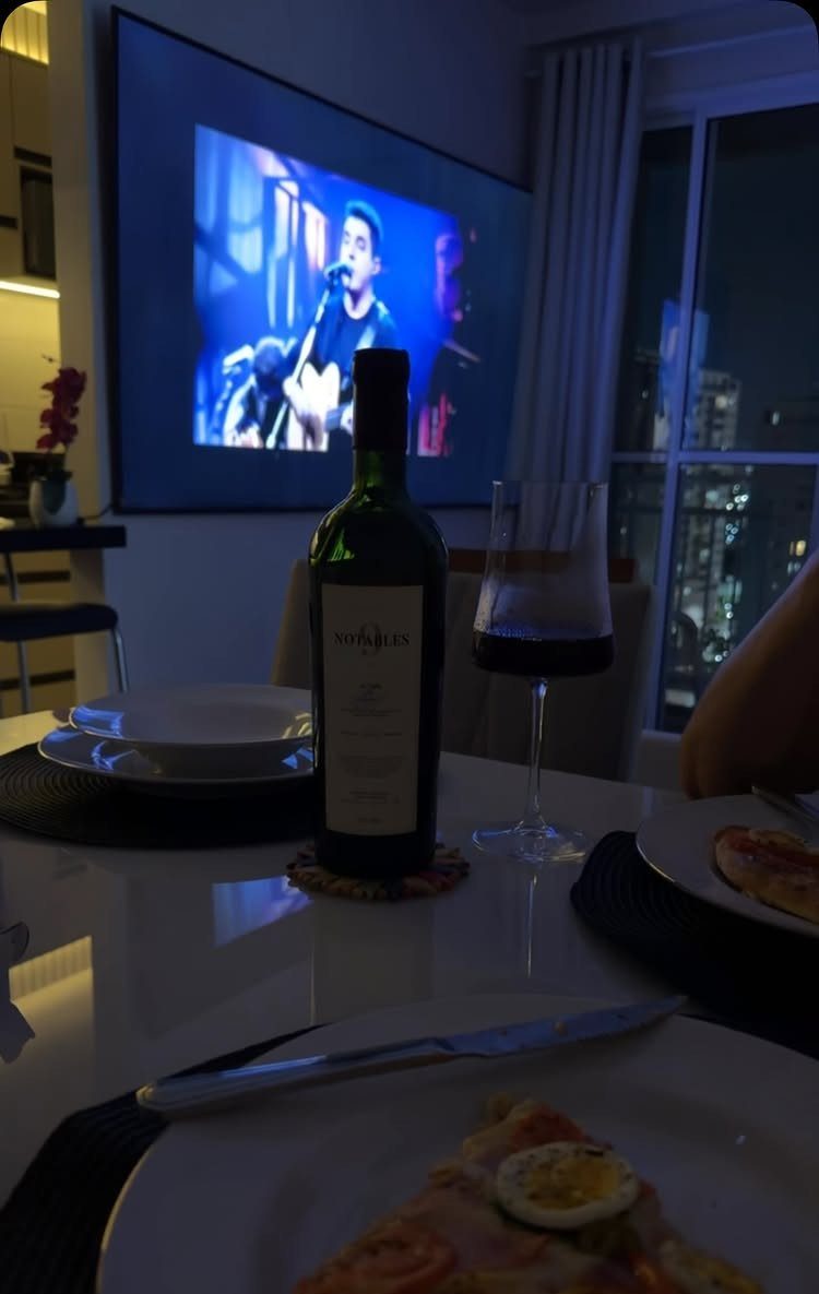 Wine bottle and glass on a table with a concert on a screen