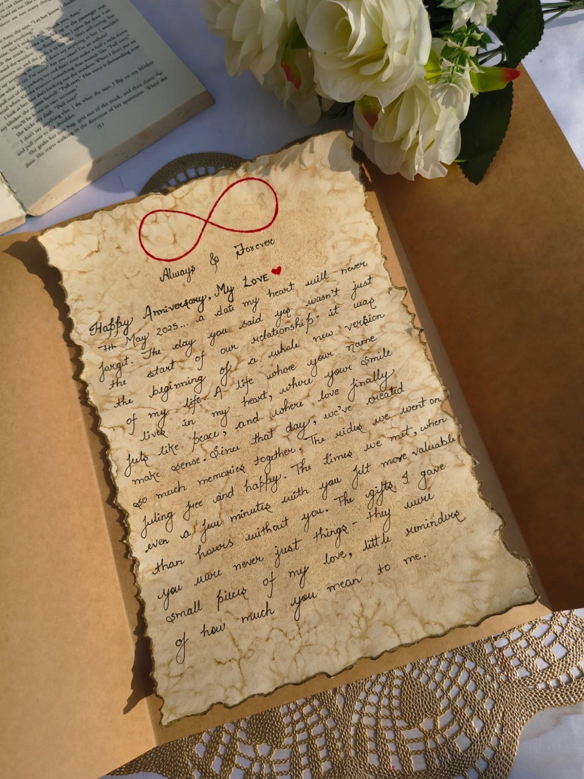 Handwritten love letter on aged parchment paper with red infinity symbol and white roses.