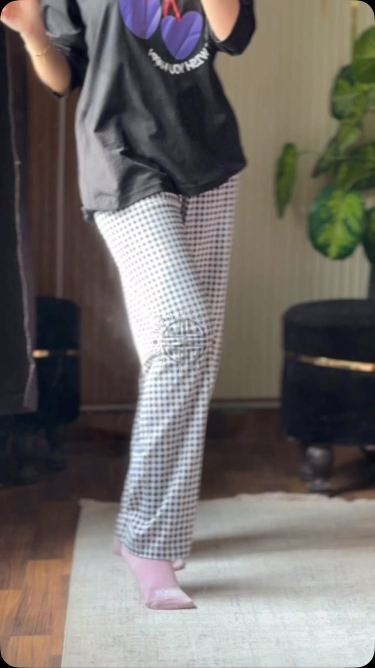 Person wearing black graphic tee and checkered soft pants with pink socks.