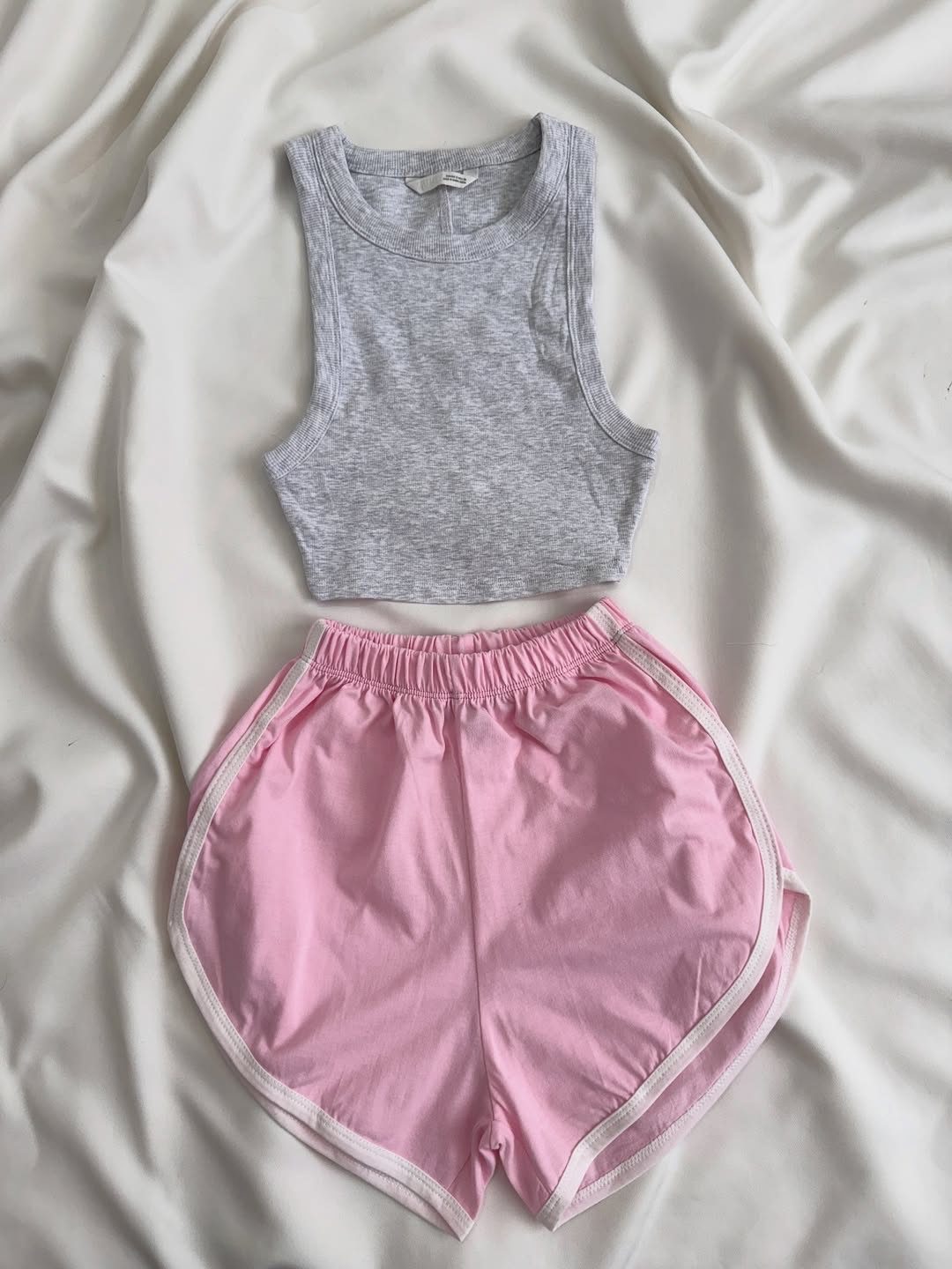 Grey tank top and pink athletic shorts laid on white draped fabric.