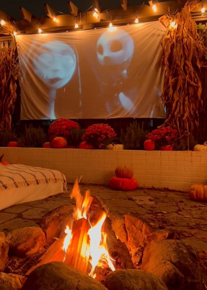 Outdoor movie screen projecting a film behind a stone fire pit and pumpkins.