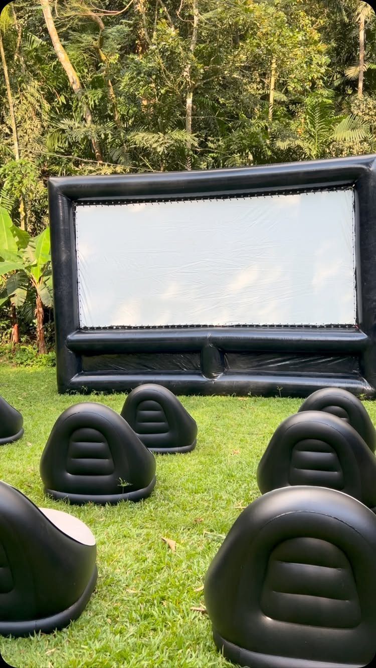 Inflatable movie screen and black bean bag chairs on a grassy lawn.