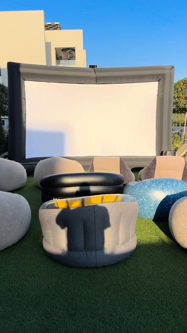Inflatable movie screen and bean bag chairs on a green lawn outdoors.