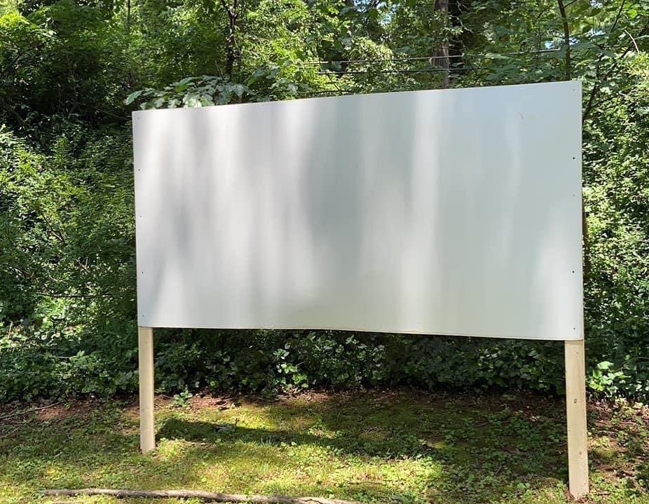 White projection screen mounted on wooden posts in a green backyard setting.