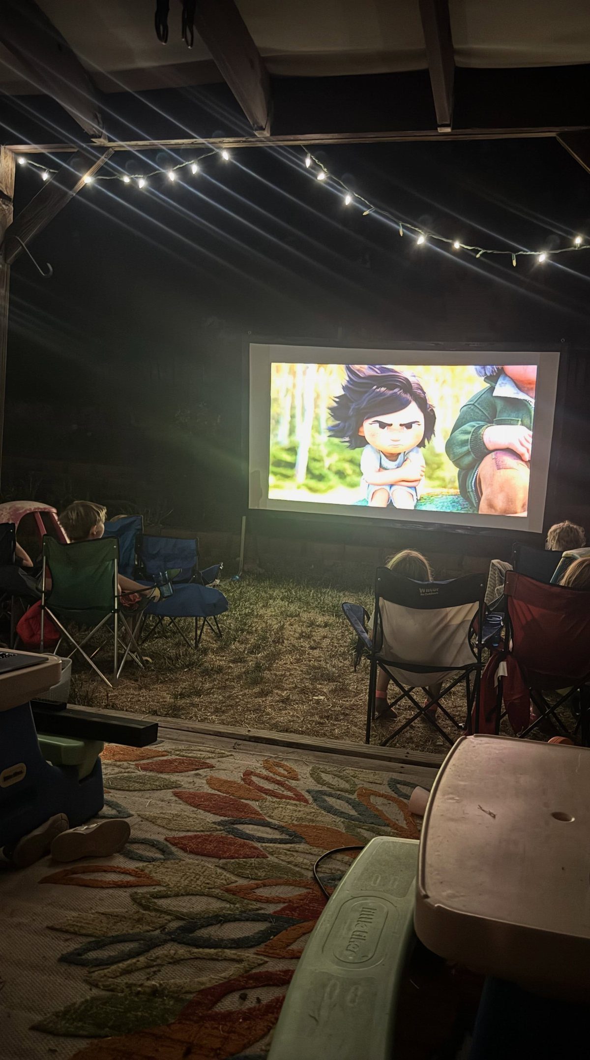 Outdoor movie screen projecting an animation for people sitting in lawn chairs.