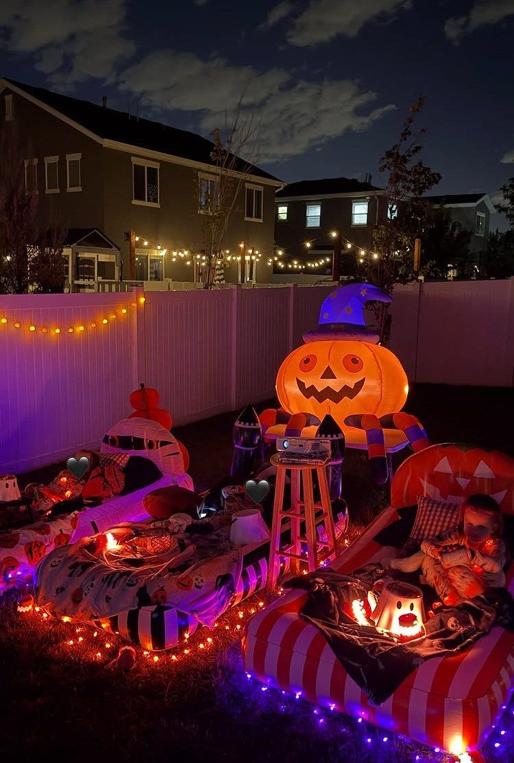 Halloween decorated backyard with inflatable pumpkin, string lights, and cozy lounge mats.