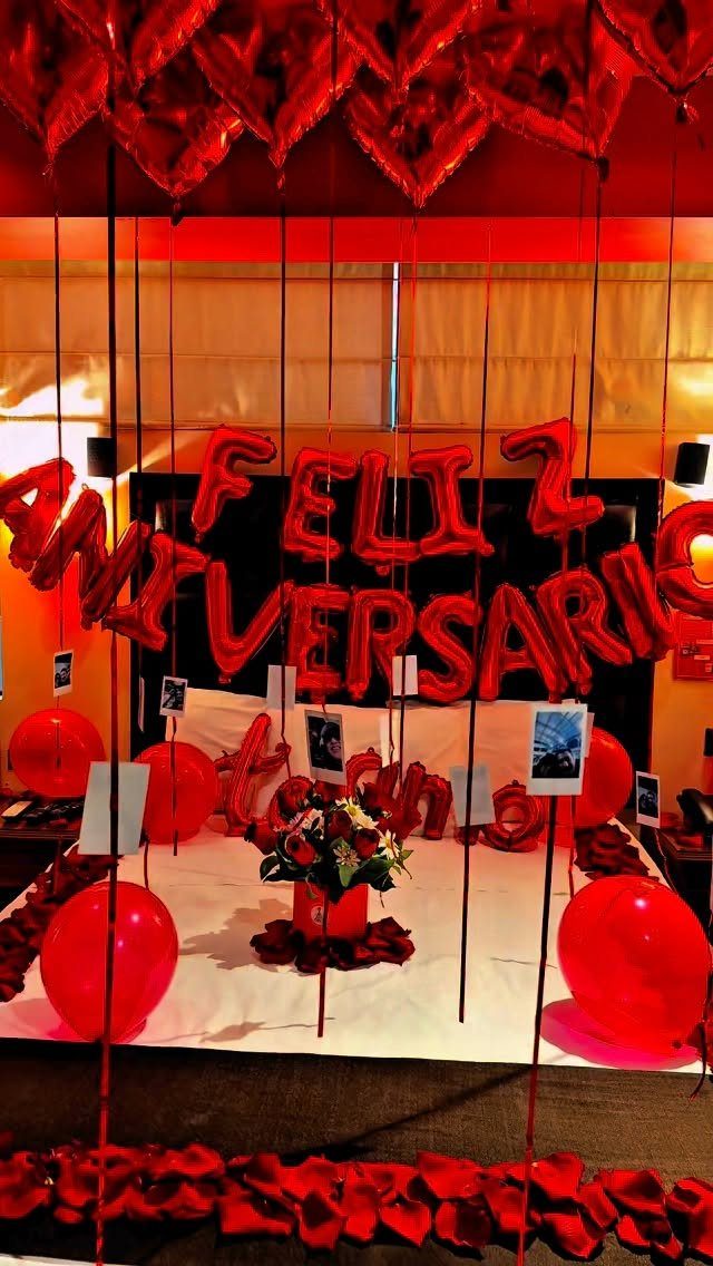 Red anniversary balloons spelling Feliz Aniversario over a bed with rose petals.